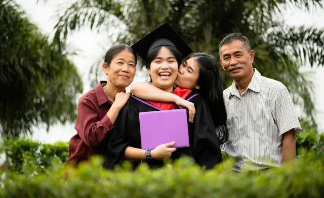 College graduate smiling and holding diploma while celebrating with family